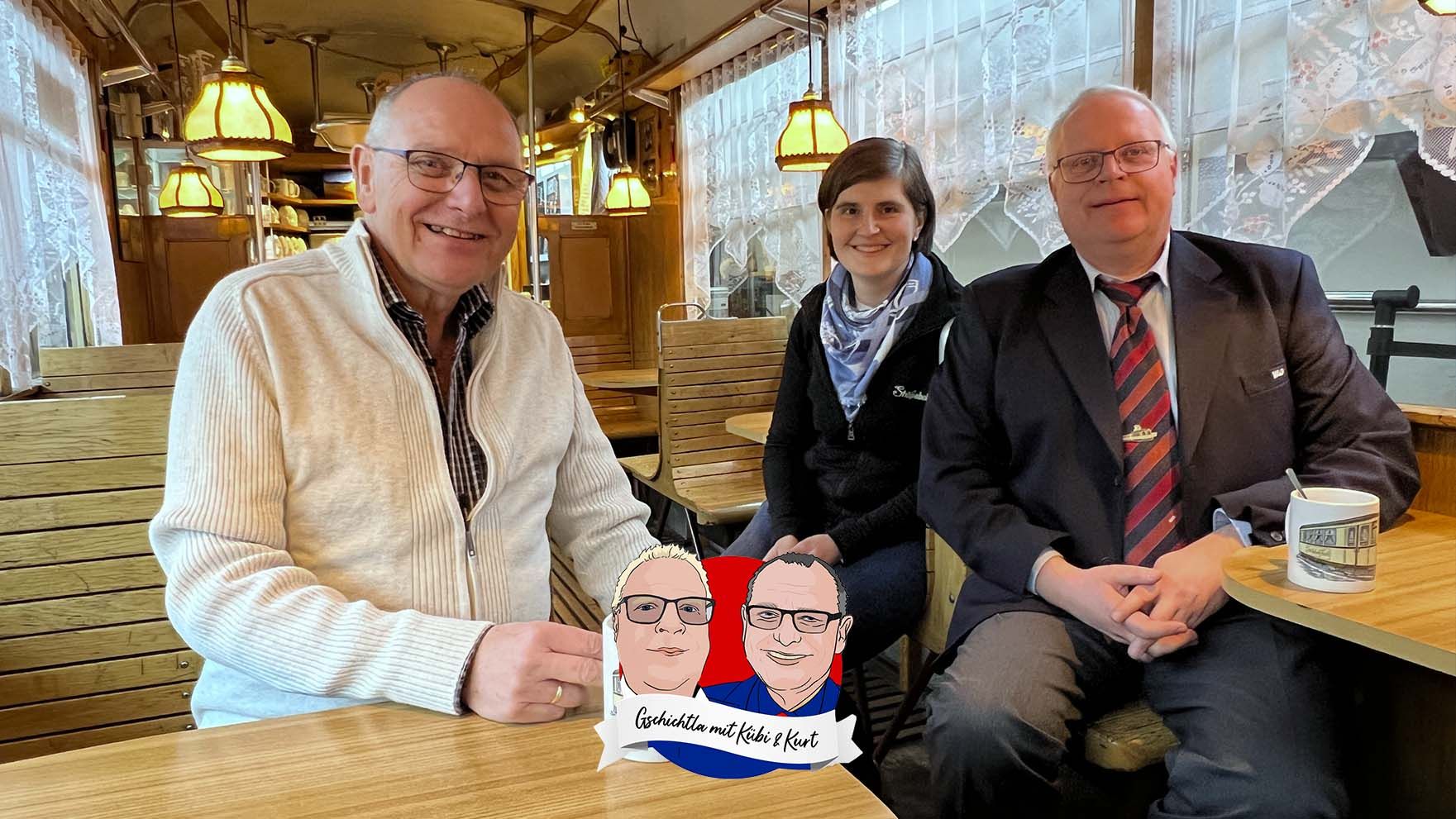 Kurt und Kübi sitzen mit ihrem Gast Alexandra in einem zum Café umgebauten Straßenbahnwagen im Depot St. Peter